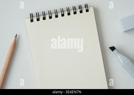 Blank spiral notebook with pencil and marker on white background, top-down view. Stock Photo