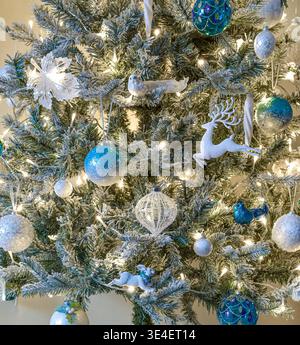 Close-up of blue and white Christmas decorations on a flocked Christmas tree with warm white lights. Stock Photo