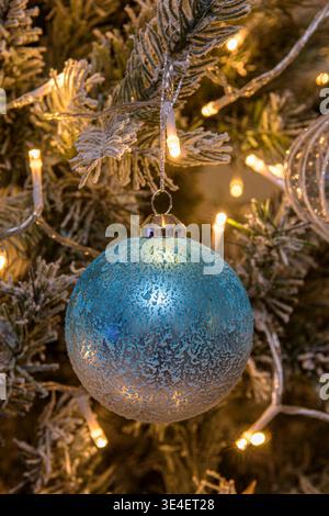 Blue Christmas bauble hanging on decorated tree with warm white fairy lights and frosted branches Stock Photo