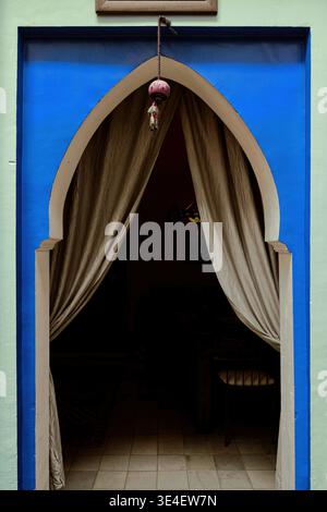 256 Horseshoe-arched doorway with satin curtain cut in a light green and blue painted wall of a traditional house in the medina. Marrakesh-Morocco. Stock Photo