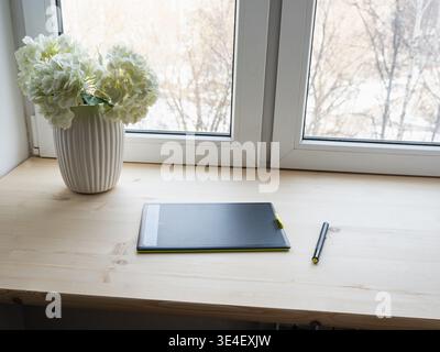 Graphic tablet and stylus on wooden desk near window with natural light for creative business and freelance work concepts Stock Photo