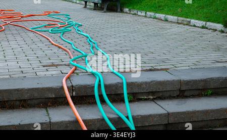 Long turquoise and orange garden hoses sprawled across a stone tile path next to a green lawn Stock Photo