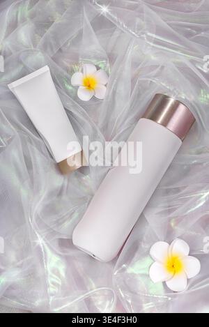 Cosmetic tubes with flowers on iridescent fabric background. Stock Photo