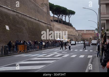 January 19, 2026, Rome, Italy: Long line of visitors queues along a high stone wall near Vatican City as pedestrians cross a city street, cars pass by Stock Photo