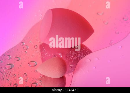 Makeup sponges with water drops on pink background. Stock Photo