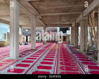 Karachi, Pakistan - Under construction Mosque  featuring concrete pillars and wooden support beams, with red prayer carpets laid out. Prayer Carpet Stock Photo