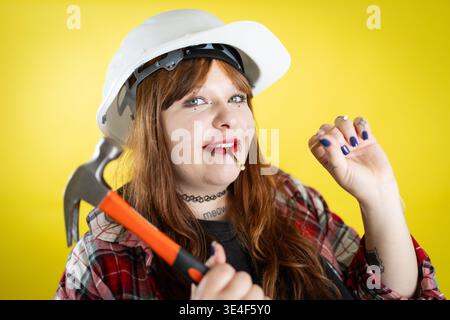 Woman wearing hard hat holding hammer with nail in mouth Stock Photo