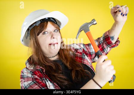 Woman wearing hard hat holding hammer ready for construction Stock Photo