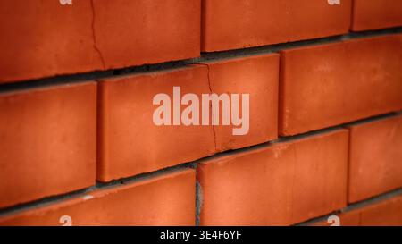 A vertical crack running through the center of several red bricks in a masonry wall. Close up. Stock Photo