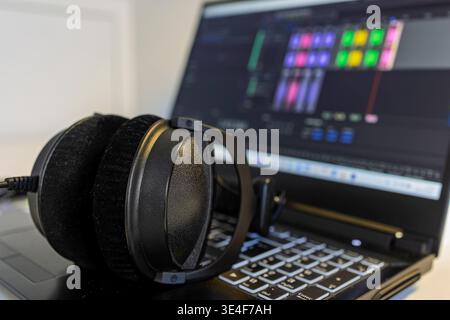 Over-ear studio headphones sitting on open laptop showing audio mixing software on screen. High angle view in bright indoor setting. Concept for podca Stock Photo