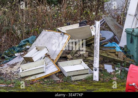 Large heap of rubbish including wooden drawers, scrap timber, and plastic debris dumped outdoors. Fly-tipping, environmental pollution, and waste mana Stock Photo