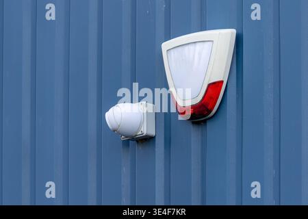 White dome CCTV camera and security siren alarm box mounted on blue corrugated metal industrial building. Property protection and surveillance concept Stock Photo