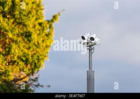 Tall white metal pole equipped with several dome and bullet surveillance cameras. Features wireless antenna at top. Clear blue sky background. Securit Stock Photo
