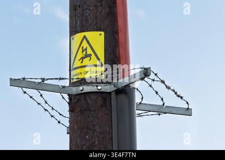 Yellow high voltage warning sign fixed to wooden pole with barbed wire. Safety and hazard concept related to electricity and restricted areas Stock Photo