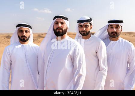 Four arab men, dressed in traditional white emirati kanduras and ghutras, standing together with serious expressions, symbolizing friendship and partn Stock Photo