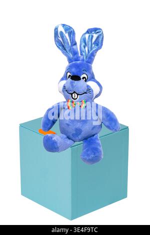 Cute blue plush bunny or rabbit with bow tie on a gift box isolated on a white background. Easter greeting card template with space for design. Bright Stock Photo