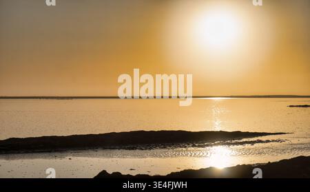 A peaceful coastal landscape showing a brilliant golden sunset over the Atlantic Ocean in Swakopmund, Namibia, with dark coastal rocks in the foregrou Stock Photo