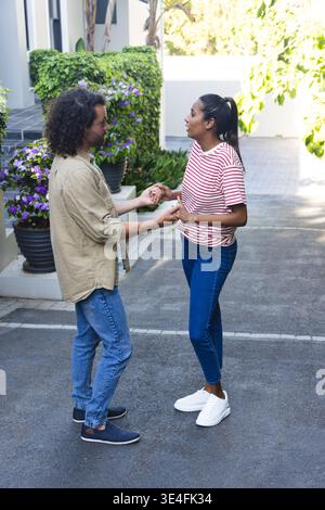 Couple holding hands and talking on paved residential driveway beside potted purple flowers Stock Photo
