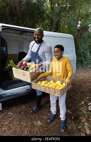 African American father in apron and son standing at van door holding vegetable crate, lemon basket Stock Photo