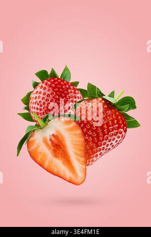 Freshly strawberry berries halves and whole soar in air with bright red flesh, green leaves on pink background. Great for summer detox menu, vitamin p Stock Photo