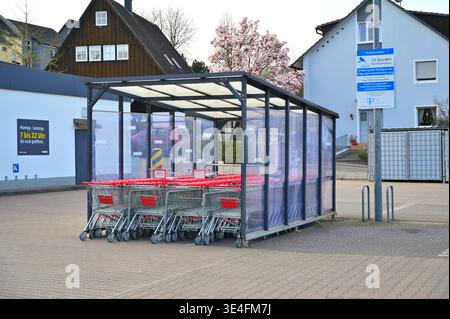 ISERLOHN, GERMANY - MARCH 27, 2026: Rows of red shopping carts in a covered outdoor storage bay at a Penny discount supermarket parking lot, surrounde Stock Photo