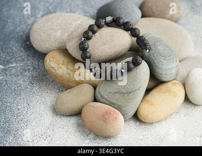 Food, Beautiful bracelet made of natural black volcanic lava. Jewelry made of round-shaped beads is placed on large sea stones. Selective focus, copy Stock Photo