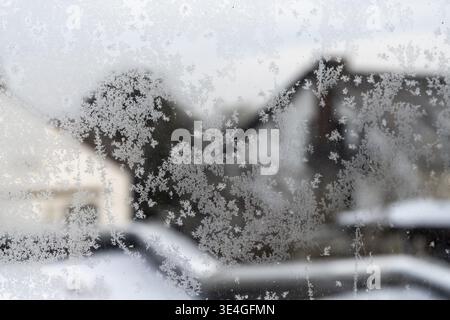Frozen window glass showing natural frost patterns with blurred winter landscape outside Stock Photo