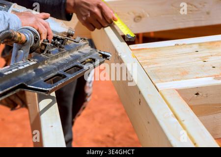 Worker cuts wood using saw while measuring with tape in construction site Stock Photo