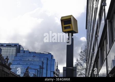 Yellow speed camera mounted on a pole in a city center. This automated device monitors traffic speed against a backdrop of modern glass buildings and Stock Photo