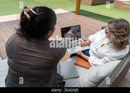 Two women engaging in a discussion while looking at a laptop computer outdoors Stock Photo