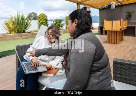 Two women of different generations learning and using a laptop on a terrace Stock Photo