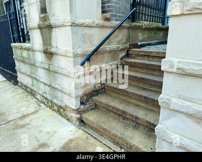 Stairs next to a building lead up from a concrete sidewalk on a cloudy day. A metal railing runs alongside the stairs. The steps show signs of wear, i Stock Photo