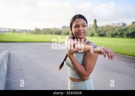 African millennial woman in sportswear stretching arms outdoors in park before workout on cloudy day Stock Photo