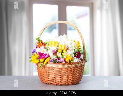 Vibrant freesia flowers in wicker basket on table against blurred window Stock Photo