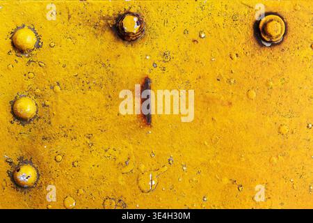 Yellow painted metal plate with rivets, rust spots, and scratches. Industrial grunge texture background with weathered surface and corrosion. Stock Photo