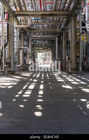 Industrial facility with steel pipes and machinery. Sunlight casts patterns on concrete floor. Long corridor gives sense of scale and order. Ideal for Stock Photo