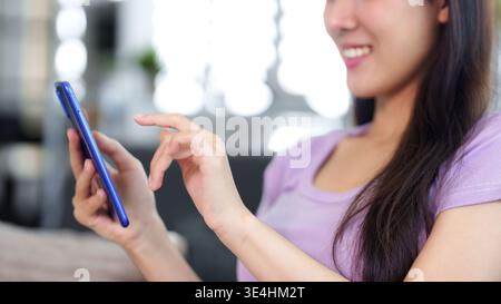 Asian woman smiling interacting with modern mobile phone. Enjoy digital content. Relaxed indoor experience. Connectivity and ease. Stock Photo