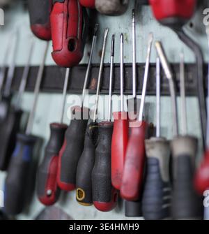 Close-up of assorted screwdrivers with black and red handles hanging in a row on a light blue wooden board, with shallow depth of field and slight bac Stock Photo