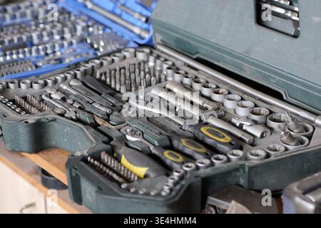 An open tool case with sockets, bits, and a ratchet is shown on a wooden surface, with selective focus on the front tools and a blurred background Stock Photo