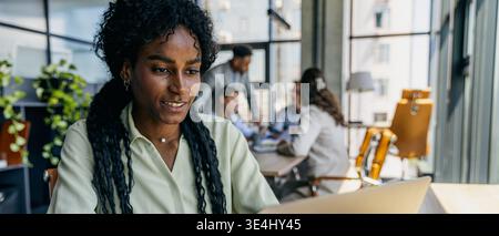 Female employee concentrating on work amid office tools and colleagues Stock Photo