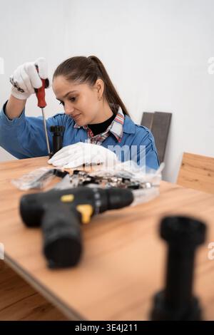 Woman furniture assembler using screwdriver tightening cabinet legs in furniture manufacturing workshop Stock Photo