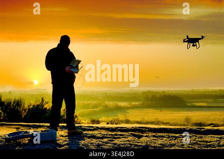 Early dawn cold winters morning test flying a new drone against  warm orange sky with low sun Stock Photo