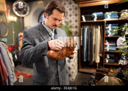 Serious handsome man customer thinking on buying fancy leather shoes in second hand vintage shop. Stock Photo