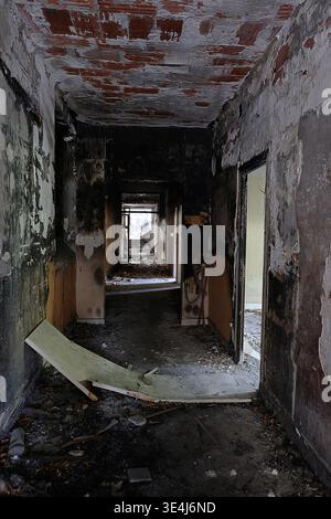 Broken door lying in the dilapidated hallway of a burned and abandoned house, dangerous place, gloomy urbex scenery Stock Photo
