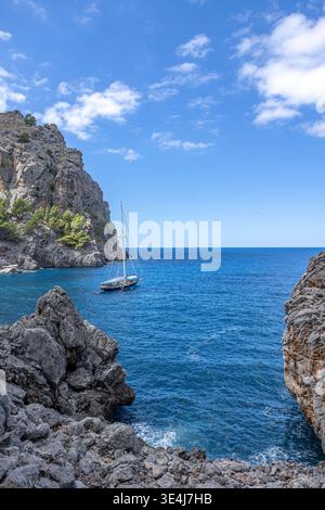 Peaceful coastal view with a sailboat floating on clear blue water surrounded by steep rocky cliffs near Sa Calobra on Mallorca west coast Stock Photo