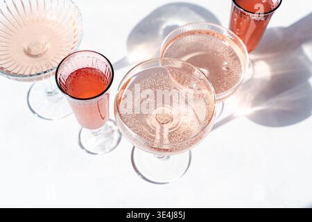 An overhead view of sparkling rose wine in elegant glassware casting artistic shadows on a white surface. The bubbly texture and sunlight create a vib Stock Photo