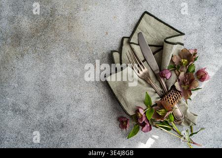 Top view of rustic spring table setting with linen napkin, fork and knife, and hellebore flowers on gray stone background with copy space for menu or Stock Photo