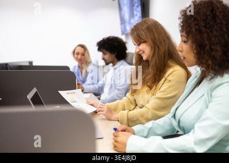 Diverse team in a modern coworking office, collaborating at shared desks with laptops, paperwork and notes. Bright workspace supports productivity, fo Stock Photo
