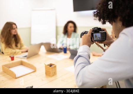 Photographer taking photos of a diverse team meeting in a modern coworking office, with laptops and notes on the table, highlighting collaboration and Stock Photo