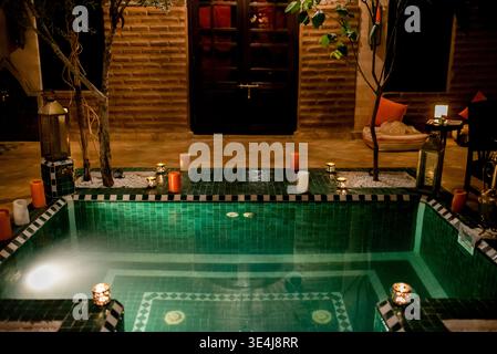 Warm candlelight surrounds a small tiled swimming pool in Morocco at night, creating a tranquil, romantic ambiance with lanterns, reflections, and coz Stock Photo